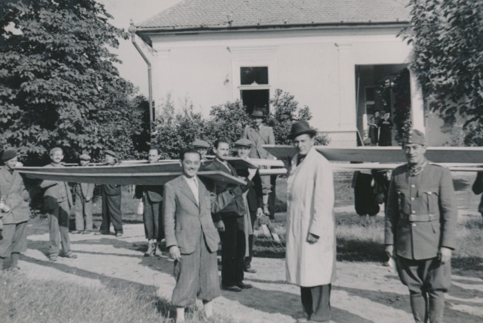 Csoportkép munkaszolgálatosokról egy ház előtt amint deszkát tartanak