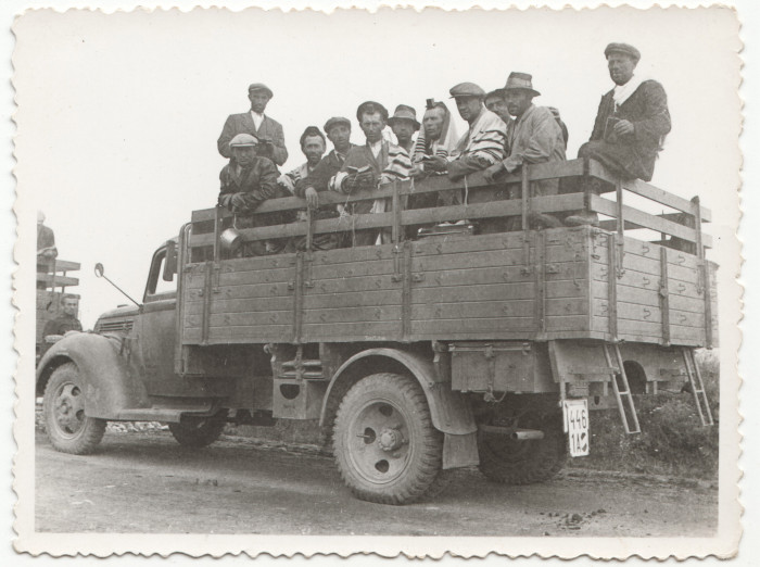Csoportkép lengyel zsidó férfiakkal egy teherautón, pár férfin imaköpeny