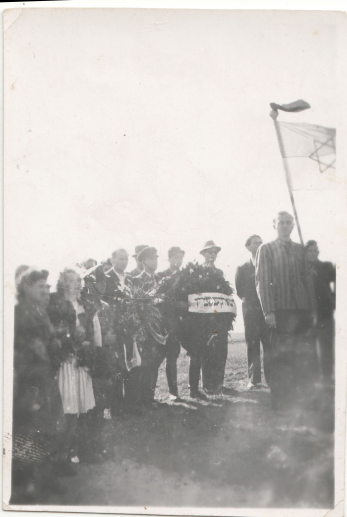 Egykori deportáltak egy volt koncentrációs tábor helyszínén zászlójukon dávid-csillaggal